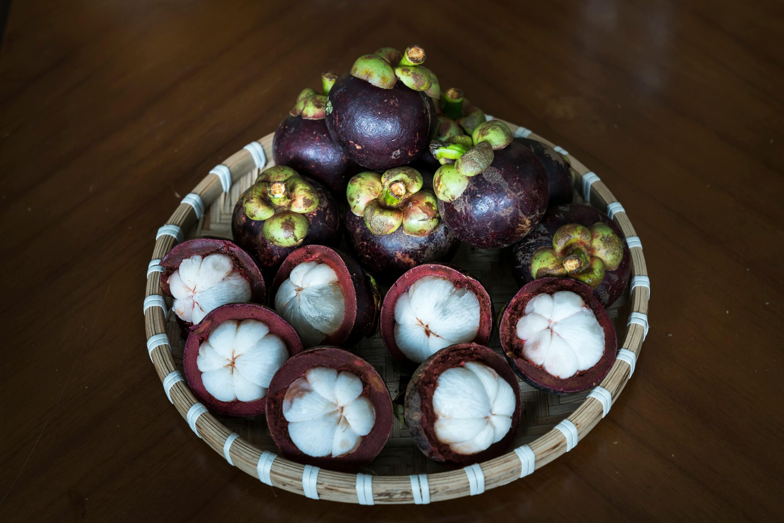 A basket of fresh mangosteen fruit displayed on a wooden table, emphasizing tropical freshness.