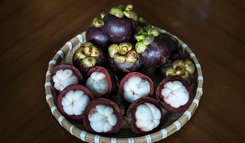 A basket of fresh mangosteen fruit displayed on a wooden table, emphasizing tropical freshness.