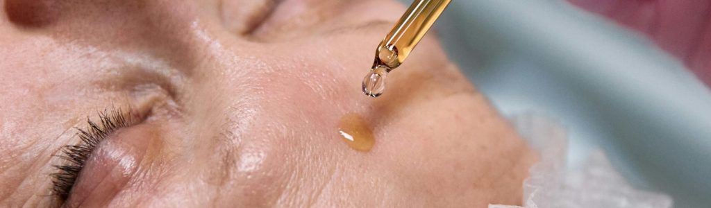 Senior woman receiving a facial serum treatment in a spa setting.